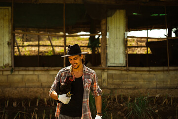 Fototapeta na wymiar Portrait of a cheerful farmer holding and taking care of chicken outdoor. A smart hipster young man holding a hen has been satisfied smiling at an organic sustainable egg farm. Vintage film style.