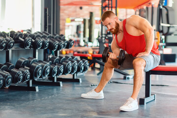 Caucasian bearded athletic man trains with dumbbells in the gym. Modern gym on the background. Concept of fitness and sport