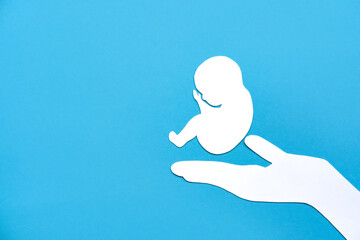 Paper silhouette of a human embryo on a doctor's hand. Flat lay, place for text.