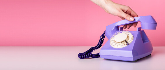 Woman hand holding retro phone handset on pink background. Banner with copy space for text.