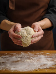 The chef holds the finished dough in his hands. Close-up. The concept is cooking dishes from dough - bread, pizza, pasta, pies, bread. Bakery, patisserie, pizzeria, home cooking, restaurant, hotel.