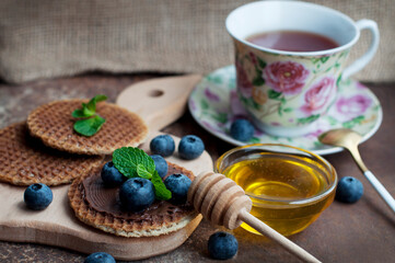 Waffles with chocolate, honey, mint, blueberries on a dark brown and canvas background. Romantic breakfast in rustic style with waffles and fruits on wooden board. 