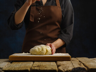 Dough prepared by the chef on a cutting wooden board. Dark background. wooden texture. minimalism. Dough products - bread, pizza, pasta, pie, confectionery.