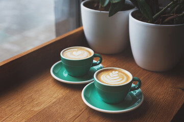 Two beautiful cups of cappuccino on the table. Decorated with perfect heart shape latte art. Coffee break, time in cafe, relax and enjoy the hot drink concept. Side view. Copy space for your text.