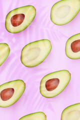 set of patterns of avocado cut in half on a light pink background with a shadow of tropical leaves