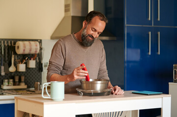 Portrait of a smiling middle-aged bearded man checking the temperature of bread dough early in the morning at home