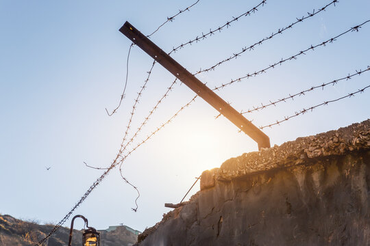 Close-up view prison or border concrete wethered fence broken old rusty barbed wire chain security barrier silhouette sky sun background. Dictatorship tyranny repression regime end freedom concept