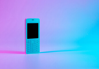 Retro cell phone vintage concept. White old mobile telephone in neon pink blue light. Retro wave....