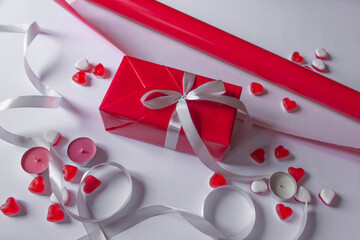 Set to gift wrapping: red paper roll and silver satin ribbon. White background with jelly hearts and candles.