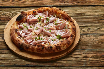 Fresh pizza with ham and pineapple on wooden table in restaurant.