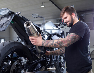 Tattooed mechanic examining exhaust pipe of motorcycle in workshop