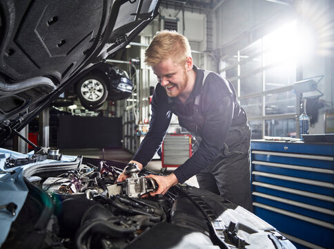 Smiling young blond mechanic repairing car engine in auto shop
