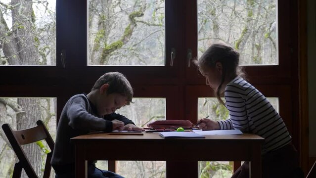 Two caucasian children are drawing near the window. Brother and sister are spending time together. High quality 4k footage