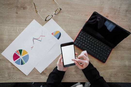 Young businesswoman using smart phone by laptop and documents on desk in office