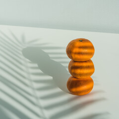 Three tangerines on a white table with the shadow of palm leaves. - 485516463