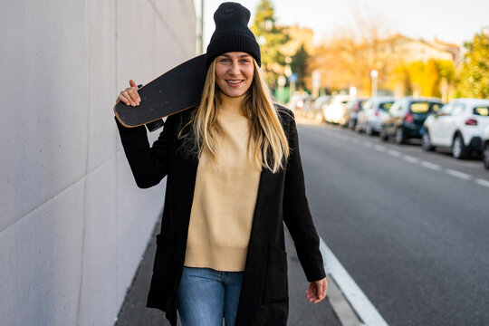 Smiling woman with skateboard walking on street