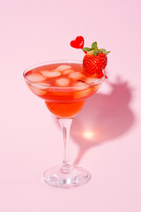 Valentine day cocktail with strawberry in martini glass on pink background