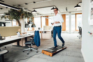 Smiling businessman running on treadmill at office