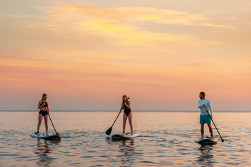 Group of caucasian people swimming on a sup boards at the ocean. Surfing with friends at the...