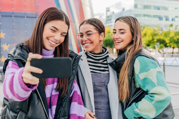 Smiling young women taking selfie on smart phone in city