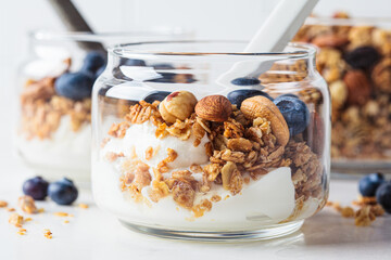 Granola with nuts, yogurt and berries in jar. Breakfast parfait with muesli, yoghurt and blueberries, white background. - obrazy, fototapety, plakaty