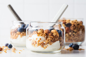 Granola with nuts, yogurt and berries in jar. Breakfast parfait with muesli, yoghurt and blueberries, white background.