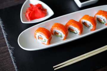Close up image of sushi roll covered with fresh salmon on the slate board.