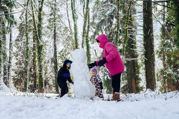 Father with daughters making snowman in winter forest