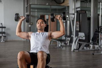Asian man exercises in fitness. Young healthy man in sportwears doing shoulders exercise in gym.