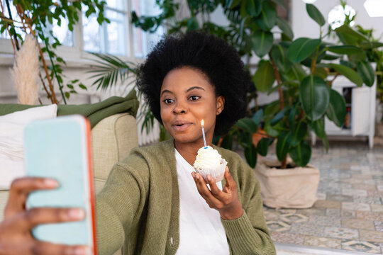 Afro woman taking selfie with cupcake in living room at home - Powered by Adobe