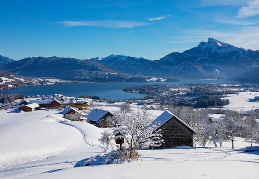 Austria, Upper Austria, Mondsee, Snowy landscape of Salzkammergut with huts in foreground and Mondsee lake in background
