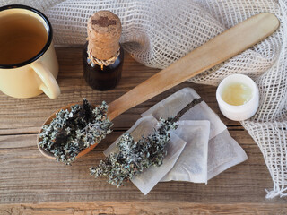 Obraz na płótnie Canvas Medicinal herb moss lichen in a spoon, tea bags, drinking extract, tea, ointment on a wooden table, top view, flat layout. Useful plant parmelia sulcata for use in medicine, homeopathy and cosmetology