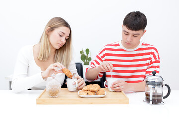 Boyfriend and girlfriend having breakfast, eating croissants and drinking coffee. Young couple at...