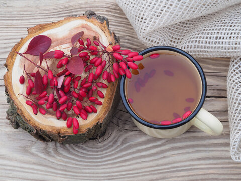 Berries and leaves of the useful berberis plant and a tea in a mug, napkin on a wooden table, top view, flat layout. Seasonal red barberry fruit and drinks for use in medicine and food