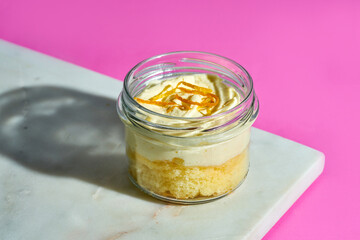 Carrot cake in a glass jar on a marble board on a pink background
