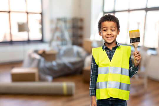building, construction and profession concept - little boy in safety vest with paint brush over home background