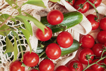 Ripe red tomatoes and fresh cucumbers are lying in net mesh bag. Top view. Fresh healthy food concept