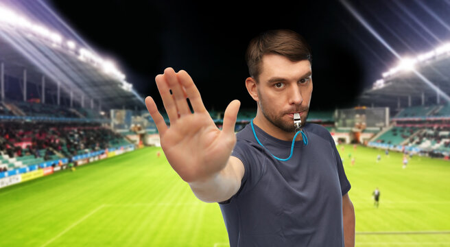 sport, football and people concept - male trainer or referee whistling whistle and showing stop gesture over soccer stadium background - Powered by Adobe