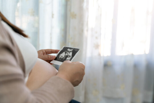 Pregnant woman holding ultrasound report at home. Mature lovely pregnant woman looking at sonogram image of her baby. x-ray pregnant.