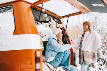 Portrait of two cheerful women friends sitting in a van in winter camp, enjoying holiday.