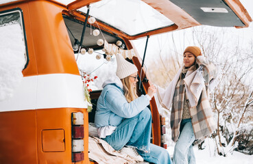Portrait of two cheerful women friends sitting in a van in winter camp, enjoying holiday.