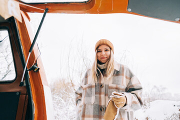Portrait of cheerful young woman standing outdoor near van in winter time.