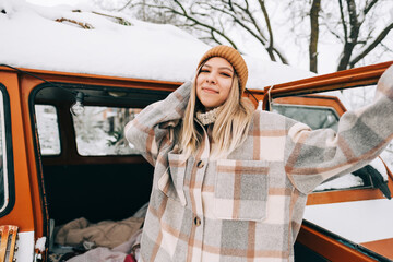 Portrait of cheerful young woman standing outdoor near van in winter time.