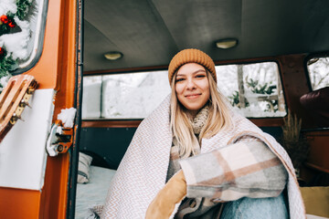 Portrait of cheerful young woman sitting in a van in winter camp.