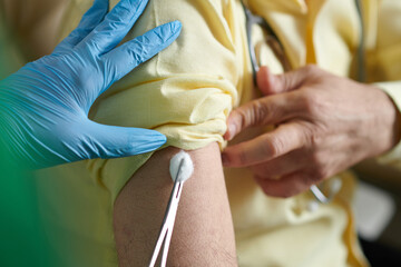 Nurse putting cotton ball on site of injection after injecting vaccine against new stamp of...