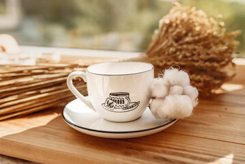 White mug on a wooden tray near the window. Cozy home, cotton and dried flowers decorations