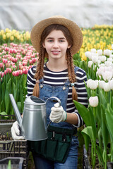 Happy smiling teenager girl in hat with watering can in blossoming tulip farm