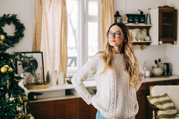 Portrait of young caucasian woman in glasses standing on the kitchen at home with Christmas...