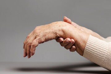 An elderly woman massages her hands, experiencing pain. Gray background, hands close-up. The...