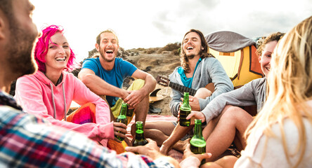 Hippie people having fun together at beach camping party - Life style travel concept with happy hipster travelers playing guitar and drinking bottled beer at summer surf camp - Warm vivid filter